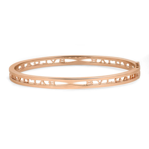 An image of a Bvlgari B.Zero1 Logo unisex adult bangle bracelet without stones. The bracelet is positioned horizontally across the center of the frame, with a slight tilt to the left side, creating a soft angle that showcases its design and the brand name inscribed on its surface. The camera angle is a direct side view, and the image is taken from a close but fully encompassing distance, ensuring the entire bracelet is in focus and visible against a white background. The bracelet is crafted from rose gold metal with cut-out details. The condition of the bracelet is new. 
