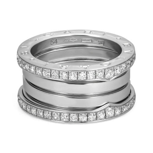 An image of a Bvlgari B.Zero1 unisex adult ring with diamonds, showcased from a close frontal angle. The ring features a four-band design with two prominent bands encrusted with diamonds in a channel setting, flanked by smooth 18k white gold polished bands. The metallic luster of the white gold-toned material contrasts with the brilliance of the diamonds. Visible engravings indicate the brand and ring size, centrally positioned in the upper portion of the image.