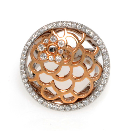 An image of a Luca Carati women's Cocktail ring with diamonds, showcased at a close frontal angle. The ring features a white and rose gold openwork band with a circular pattern, topped by a round, diamond-encrusted bezel setting. The intricate design includes a central floral motif with diamond accents, surrounded by a halo of smaller diamonds, providing a contrast against the polished metal. The image is taken from a distance that captures the entire ring, allowing the ornate details and sparkling gems to be clearly visible.