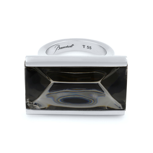 An image of a Baccarat So Insomnight branded women's ring with Mordore crystal. The ring comes with rectangular Mordore crystal in the center, featuring the Baccarat logo is centered in the image. The ring is new with defect, minor crack on the edge of the crystal. The ring is photographed from a front angle, showcasing the top view of the lid with the size inscription "T 55" visible. The photo is taken from a close distance, with a focus on the ring, suggesting the ring is inside. 
