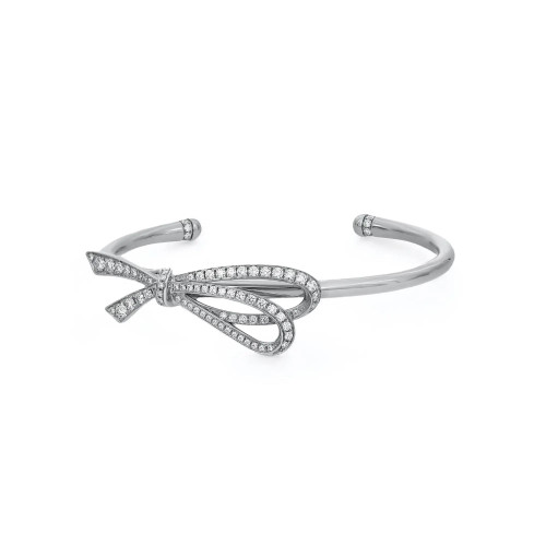 An image of a Tiffany & Co. women's bracelet with diamonds, positioned centrally on a plain white background. The bracelet is viewed from an overhead angle at a close distance, showcasing its intricate bow design with round cut diamond embellishments in white gold. The open cuff style allows for a glimpse of the wrist it would adorn, and the metallic sheen contrasts with the sparkle of the precisely set stones.