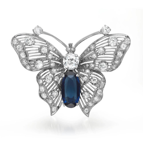 An image of a Rachel Koen unisex adult brooch with diamonds and synthetic blue sapphire set in a white gold. The brooch is crafted in the shape of a butterfly with outstretched wings, adorned with multiple sparkling diamonds of various cuts and sizes. The view is head-on, displaying the brooch's symmetrical design with the butterfly facing upwards. The photo is taken from a close distance, capturing the intricate details and the reflective quality of the materials.The brooch is pre owned in a great condition. 