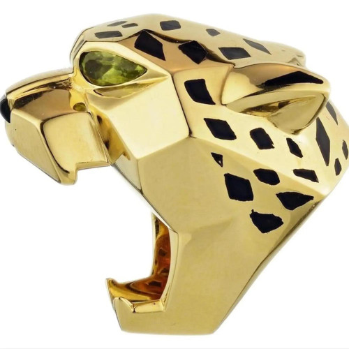 An image of a Cartier women's ring styled in the shape of a leopard's head, featuring a polished yellow gold with black lacquer spots and a striking green peridot gemstone for the eye and onyx nose. The ring is shown in a close-up view with the leopard's head angled slightly to the left, highlighting the contours and craftsmanship of the design. Great preowned condition.