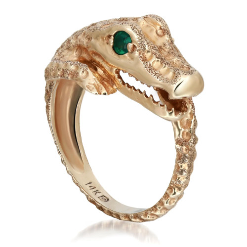 An image of a unisex adult ring by Rachel Koen, featuring a crocodile design. The ring is crafted in yellow gold with detailed texturing, forming the shape of a crocodile head with an emerald gemstone eye. The image shows a side view of the ring, capturing the intricate details and open mouth design from a close-up angle. The ring is positioned upright, showcasing the 14K hallmark on the inner band.
