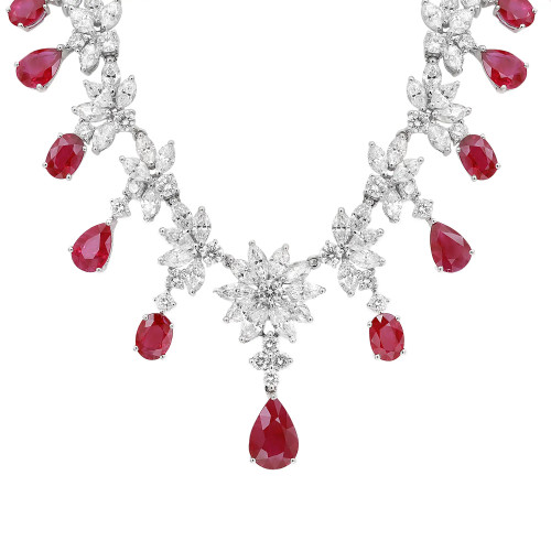 An image of a Rachel Koen women's necklace featuring diamonds and rubies. The necklace is displayed from a front angle at a close distance, highlighting its intricate design in white gold. It showcases a series of diamond clusters, resembling floral patterns, interspersed with large, teardrop-shaped red ruby gemstones. The arrangement creates a symmetrical and elegant appearance. Excellent preowned condition.