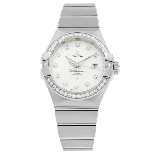 An image of a women's OMEGA Constellation wristwatch, displayed front-facing and centered at eye level. The watch features a white gold band and a round dial with diamond hour markers. The bezel is adorned with additional diamonds, and the date is visible at the 3 o'clock position. The watch is a display model, shown at a close-up angle to highlight its details.