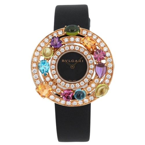 An image of a pre-owned women's Bvlgari Asutorare Cherki 18K Yellow Gold Gemmed Diamond Watch AE36G taken from a front-facing angle at a close distance. The watch features a black strap and an ornate, circular face adorned with colorful gemstones and a ring of diamonds surrounding the black dial.