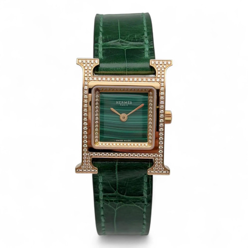 An image of a pre-owned HERMÈS Heure H 21mm 18K Rose Gold Diamond Green Malachite Dial Watch HH4.272, displayed from a front-facing angle. The timepiece features a square, gold-toned case encrusted with diamonds, highlighting its luxurious design. The watch has a green malachite dial with matching green leather strap. Photographed at a close distance to capture intricate details.
