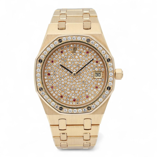 An image of a pre-owned Audemars Piguet 36mm Yellow Gold Rubies Diamond Dial 14813BA women's wristwatch, viewed from a slightly elevated front angle. The watch features a yellow gold case and bracelet, with a bezel and dial adorned with numerous small diamonds. A date indicator is visible on the right side of the dial. The watch is close-up, showcasing its luxurious details.
