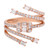 An image of a Rachel Koen women's ring with diamonds, displayed against a white background. The rose gold ring features an intricate spiral design with multiple bands intertwining at varying angles. It is adorned with numerous small round-cut diamonds along the bands and larger baguette cut diamonds set at intervals. The ring is captured in a close-up view, showcasing the sparkling facets of the diamonds and the polished finish of the metal.