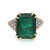 An image of a Rachel Koen women's cocktail ring with a large, central emerald-cut emerald set in a  18k yellow gold band. The emerald has a rich, deep green color and is held by four gold prongs. Flanking the central stone on both sides are triangular clusters of small, round-cut diamonds, creating a sparkling contrast. The ring is photographed from a top view at a close distance, showing off the facets of the emerald and the shine of the metal. The condition of the ring is pre owned. 
