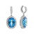 An image of a pair of Rachel Koen women's 14k white gold drop earrings featuring oval-cut blue Topaz surrounded by halos of diamonds. The left earring is shown front-facing, displaying the topaz faceted surface and the sparkling diamonds. The right earring is viewed from a side angle, revealing the depth of the earring and the profile of the blue topaz with a reflective pattern behind it. Both earrings are positioned against a white background and are shown in close-up to highlight the details. The condition of the earrings are pre owned. 