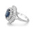 An image of a Rachel Koen women's ring featuring diamonds and blue sapphire. The ring is centered and displayed at a slight left angle, showing off the large, oval-shaped blue sapphire in the middle, which is surrounded by a halo of baguette and round-cut diamonds. The band is made of polished 14K white gold, highlighting the intricate design and luxurious appearance. The close-up view provides a clear perspective of the ring's details and craftsmanship.