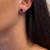  Front and side image of the pair of stud earrings with large, oval-cut central ruby surrounded with halo round cut diamonds that creates a classic flower-like silhouette set on a white gold setting worn on left ear of a woman