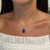 Front view of the necklace on models neck showing the oval cut prong set blue tanzanite with round cut diamonds pendant with yellow gold link chain