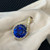 Front view of the pendant showing the prong set blue tanzanite stone in the center accented by pave and prong set round cut diamonds in yellow gold placed on the cloth
