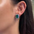 Front view of the emerald cut emerald and round diamond stud earrings on model's ear showing the perfect fit and size of the earring on the ear.