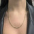 An image of a simple, elegant Rachel Koen necklace without stones, displayed on an unisex adult model. The necklace features a yellow gold twisted chain design and rests just below the collarbone. It is shown from a frontal view with the model wearing a black leather jacket, with the focus on the necklace and the upper chest area. The image is taken from a medium distance and a straight-on angle, providing a clear view of the necklace's design and how it lays on the skin. The condition of the chain is pre owned. 