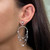 An image of a Messika diamond earring for women, featuring a close-up side view of the left ear. The earring is composed of concentric teardrop shapes adorned with multiple diamonds, creating a cascading effect. The earring is worn on the lobe, with the largest teardrop positioned at a slight angle away from the face, giving a sense of depth and dimension. The diamonds catch the light, emphasizing their intricate setting and the earring's elegant design.