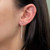 An image of a Messika earring with diamonds, designed for women, displayed on an ear. The earring features a linear drop style with multiple small diamonds set in a vertical row, giving a delicate sparkle. The earring hangs straight down from the lobe and is viewed from a side angle, providing a clear view of its length and design.