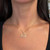 An image of a delicate Messika necklace with diamonds, designed for women. The necklace is centered and worn around the neck, positioned just above the collarbones. The pendant, featuring a sparkling diamond-studded design, hangs at a close-up angle, providing a clear view of its detail and craftsmanship. The necklace chain is visible, draping gracefully with small, evenly spaced diamonds adding to its elegance. The background is a close view of the wearer's neck and upper chest, putting focus on the necklace.