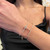 An image of a woman's wrist adorned with an elegant Messika bracelet with diamonds. The bracelet features a delicate chain with a central diamond-encrusted circular motif. The image is taken from a close, slightly elevated angle, focusing on the top of the wrist to showcase the jewelry's design and sparkle. The background is softly blurred, drawing attention to the bracelet.