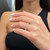 An image of a Messika brand ring with diamonds displayed on a woman's finger, centered and in sharp focus. The ring features several prominent diamonds set in a rose gold band. It is viewed from a side angle, showcasing the sparkle of the diamonds and the design of the band. The background is blurred, with the ring being the main object of attention at a close but comfortable distance, allowing for detailed observation of its design and craftsmanship.
