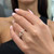 An image of a woman's hand wearing a Messika diamond ring, viewed at a close angle. The ring, designed for women, features multiple small diamonds arranged in a geometric pattern on a band that is visible on the ring finger. The hand is in focus with the nails painted light pink, and the background is softly blurred.