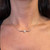 An image of a Messika brand necklace with diamonds, designed for women. The necklace is positioned centrally around the model's neck, with a close-up view that focuses on the necklace while showing the model's neck and collar area. The diamond pendant is prominently displayed at the center of the necklace, catching the light at a straight-on angle. The chain of the necklace extends symmetrically on both sides, leading to the edges of the image at a medium distance, providing a clear view of the jewelry's design and sparkle.