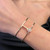 An image of a Messika brand women's bracelet with diamonds, displayed on a wrist at a close-up angle. The bracelet features a sleek, rose gold band with a prominent diamond circle centerpiece, reflecting light from its finely cut stones. The view is focused on the top of the wrist, showing the bracelet in a horizontal position that highlights its elegance and shine.