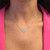 An image of a Messika brand necklace with diamonds, designed for women, displayed on a model's neck. The necklace features a central ornate diamond-encrusted pendant with a symmetric filigree design, flanked by smaller diamond accents along the chain. The view is a close-up, centered front shot, focusing on the necklace which sits against the model's skin with a pink top in the background. The angle of the photograph is straight-on, capturing the sparkle of the diamonds and the intricate detailing of the pendant. The distance is such that the necklace and the upper chest area of the mannequin are clearly visible, providing a detailed view of the jewelry piece.
