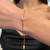 An image of a Messika bracelet with diamonds worn on a woman's wrist. The bracelet is positioned in the center of the wrist and is in sharp focus, highlighting a circular diamond feature with a halo design. The wrist is angled slightly, with the hand pointed down, and the bracelet dangles elegantly, showcasing its length and delicate chain. The distance is close-up, providing a clear view of the bracelet's design and the sparkling diamonds against the woman's skin. The background is blurred with the woman's attire visible but not in detail, ensuring the bracelet remains the central point of the image.