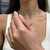 An image of a woman's hand elegantly displaying a Messika ring with diamonds. The ring, intended for women, features a yellow gold band adorned with triangular diamond settings. The hand is positioned at a three-quarter angle with the ring in clear focus, giving a detailed view of the ring's design. The distance between the camera and the ring allows for a close-up that captures the sparkle of the diamonds and the fine craftsmanship of the ring. The woman's fingernails are painted a light pink shade, complementing the overall sophistication of the image.