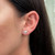An image of a triangular-shaped Messika diamond earring worn on the lobe of a woman's left ear. The earring is in clear focus and is positioned at a slight angle, showcasing the brilliance of the diamonds. The camera is at a close, but comfortable distance, ensuring the earring's details are visible against the skin, with the ear and part of the wearer's dark hair framing the piece.
