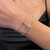 An image of a Messika women's Manch Glam'Azone bracelet with diamonds, worn on the left wrist. The bracelet features a double-band design with a central circular diamond charm, viewed from a close angle that highlights the sparkle of the stones against the wearer's skin. The image is taken from a side perspective, focusing on the bracelet with a blurred background.