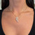 An image of a Messika women's Angel necklace with diamonds, displayed on a person's neck. The necklace features a delicate chain and a wing-shaped diamond pendant centered at the collarbone. The pendant has multiple diamonds arranged in a tapered pattern, creating a feathered effect. The photograph is taken from a front view at a close distance, emphasizing the sparkle and design of the diamonds against the backdrop of the wearer's skin and black top.