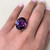 Top view of the ring on model hand showing the perfect fit on finger and the oval cut synthetic sapphire stone with four prongs and three round diamonds on both sides in yellow gold.