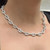 An image of a diamond necklace by Rachel Koen worn by a woman, shown in close-up. The necklace features intricate links with multiple diamonds made in 18K white gold and is positioned around the neck, visible from a left angle, highlighting its sparkle and design. The distance is close enough to show the necklace's details while also showing the neckline of the wearer.