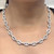 An image of a Rachel Koen diamond necklace, designed for women, displayed on a neck model. The necklace is made in 18K white gold and features a series of interlinked diamond-encrusted oval shapes with a close-up, centered view, positioned at a straight angle to show the necklace's full length. The distance is such that the necklace and part of the neck are in clear focus, filling the frame to highlight the jewelry's design and sparkle.