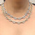 An image of a Rachel Koen women's necklace with diamonds is displayed on a person's neck. The luxurious necklace features oval shaped links, each encrusted with sparkling round cut diamonds. It shows two necklaces with the same design in yellow and white gold. The shot is a close-up, taken from a front-facing angle, with the necklace occupying the central portion of the frame, focusing on the shine and intricate detail of the jewelry.