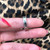 An image of a Bvlgari B.Zero1 unisex adult ring without stones, displayed on a finger. The ring is in clear focus, positioned at the center of the frame at a close distance, showcasing a frontal view with the band's edges slightly angled towards the camera. The background features a blurred leopard print pattern.The condition of the ring is pre-owned. 