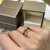 An image of a unisex adult Bvlgari B.Zero1 two band ring without stones, worn on a finger, displayed at a close distance and a slight angle, showcasing the ring's design and engravings. In the blurred background, a Bvlgari box is partially open, suggesting the product's brand authenticity.The condition of the ring is new. 