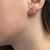 An image of a Bvlgari Bvlgari round cut stud earring with diamonds, designed for women, worn on the left ear. The earring is captured from a side angle focusing on the earlobe, with a close-up view that emphasizes the jewelry's details against the background of the wearer's skin. The gold setting encircles a central diamond, with the earring's texture and shine prominently displayed.The condition of the earrings are new. 