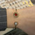An image of a Bvlgari Classic women's bracelet with carnelian and mother of pearl, worn on the wrist. The bracelet is displayed at a close distance and a slight angle, showcasing the top view of a round red carnelian gemstone encircled by the engraved brand name on one end, with a similar design featuring a mother of pearl gemstone on the other end. The band is rose gold and the wrist is partly covered by a gray sleeve with white stitching.The condition of the bracelet is new. 