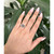 An image of a Chopard diamond ring for women, showcased on a person's ring finger. The ring is viewed from a top-down perspective at a close distance, emphasizing the ring's design and the sparkle of its diamonds. The hand is slightly tilted towards the camera, giving a clear view of the ring set against the backdrop of green foliage. The image captures the ring in good lighting, highlighting its details and craftsmanship. The ring is pre-owned in a great condition.