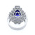 An image of a Rachel Koen brand women's ring with diamonds, captured from a top view angle showcasing the intricate design. The ring features a prominent blue tanzanite at its center, surrounded by an ornate white gold filigree setting studded with small diamonds. The band is visible below, reflecting light on its polished surface. The photo is taken from a close distance, ensuring that the details of the ring's craftsmanship are clearly visible.