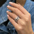 An image of a woman's hand adorned with a Rachel Koen ring featuring diamonds, viewed from a close, slightly elevated angle that focuses on the ring positioned on the ring finger. The hand is resting against a blue denim background, with the fingers slightly curled, enhancing the sparkle of the diamonds.The ring is pre owned in a great condition.