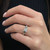 An image of a Rachel Koen women's ring with diamonds, showcased on a person's finger which is in focus. The ring is positioned roughly at the center of the frame, with a close-up side view that highlights the brilliance of the diamonds. The hand is slightly angled towards the camera, allowing a clear view of the ring's design and the sparkling stones from a short distance, set against a blurred dark background.The ring is pre owned in a great condition.