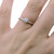 An image of a Tiffany & Co. engagement ring with diamond, showcased on a woman's ring finger. The ring is positioned at a frontal angle with the diamond facing directly towards the camera, offering a close-up view that emphasizes the ring's design and the diamond's brilliance. The platinum band is slender and smooth, leading up to the single, prominent round-cut diamond set in a classic six prong setting. The image is taken at a close distance, providing clear detail of the ring against the skin of the finger.