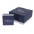 An image of a Bliss by Damiani brand jewelry box and booklet, without the necklace visible. The square box is dark blue with sparkles and features the Bliss logo in silver on the top. Positioned on a white surface, the box is shown from a front angle and appears closed, centered in the frame. A matching dark blue booklet with the word "bliss" on the cover is placed to the left of the box, partially open to reveal multiple pages. The focus is on the box, suggesting the necklace with diamonds is inside, although the necklace itself is not shown.